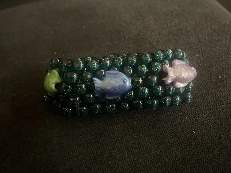 A bracelet with five rows of sparkly teal beads and colorful fish beads woven in