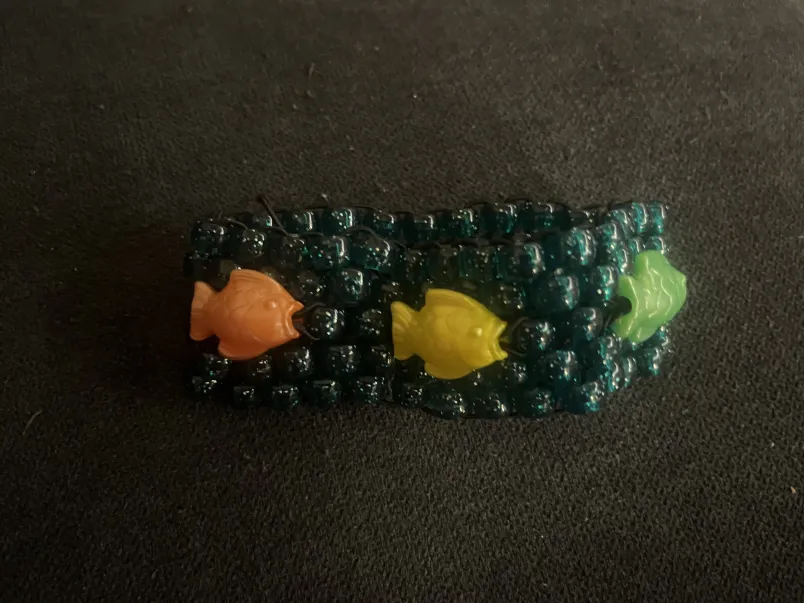 A bracelet with five rows of sparkly teal beads and colorful fish beads woven in
