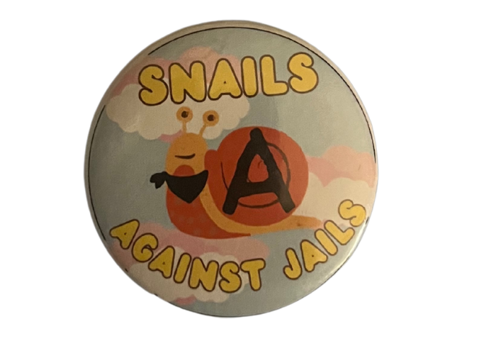 a button that reads 'snails against jails.' Features a snail wearing a black bandana around its neck with a black anarchy symbol on its shell.