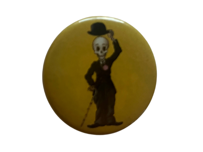 a button featuring a skeleton wearing a suit and tipping a bowler hat. They hold a bamboo cane.