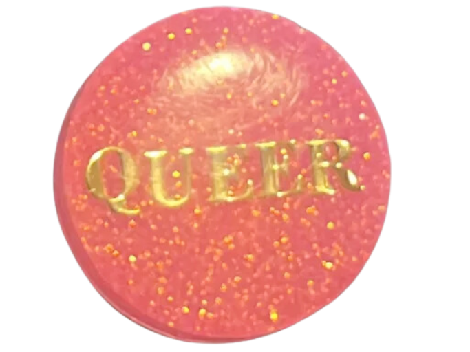 pink sparkly pin that reads 'queer'.