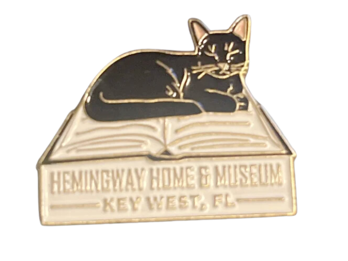 pin of a cat laying on an open book that reads 'Hemmingway Home and Museum. Key West, FL.'